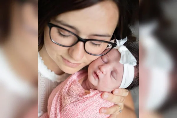 Foto colorida de uma mulher vestida de branco, segurando um bebê vestido de rosa - Metrópoles