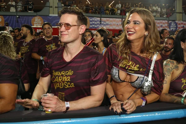 Na fotos duas pessoas aparece assistindo a um desfile de uma escola de samba na Marquês de Sapucaí