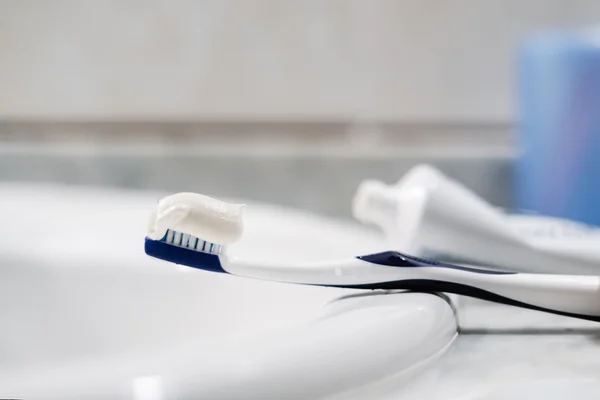 Foto em close-up mostra uma escova de dentes numa pia de banheiro com pasta de dente sobre ela - Metrópoles - Creme dental Colgate