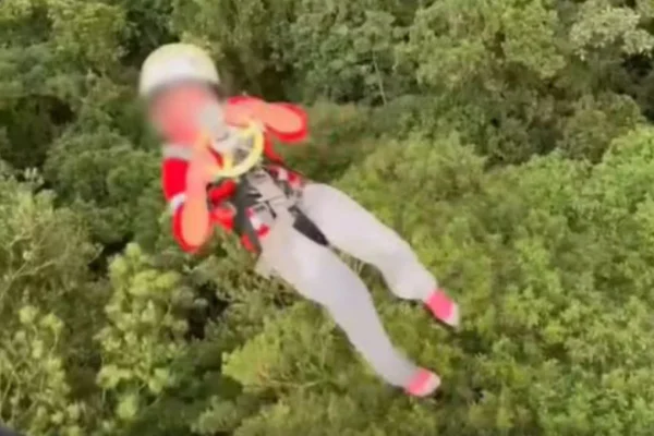Imagens coloridas mostram uma criança com o rosto borrado presa a um cabo em resgate de helicóptero em uma mata