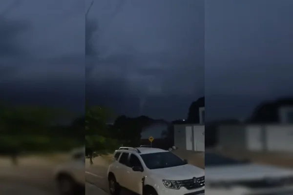 Imagem mostra o temporal ao fundo da imagem e um carro branco centralizado.