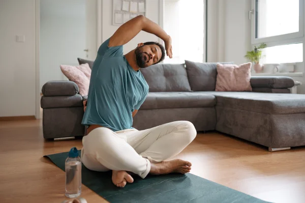 O homem se exercitando sozinho em casa, esticando as costas e o braço. Treino solo em casa e meditação, rotina de exercícios matinais ou noturnos