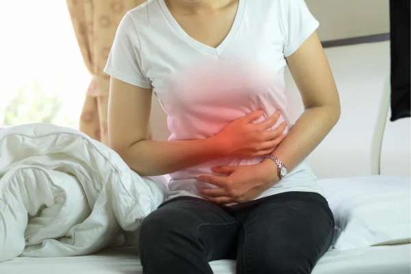 Mulher leva as mãos ao intestino como sinal de dor - e esse é um dos sintomas da Síndrome do Intestino Irritável