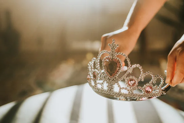 As mãos de uma criança entrando no quadro e pegando uma tiara de plástico prateada brilhante, coberta de joias de plástico. Conceito princesas da disney