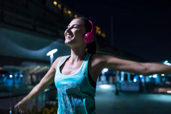 Foto colorida de mulher com fone rosa e blusa azul. Ela está com os braços abertos - Metrópoles