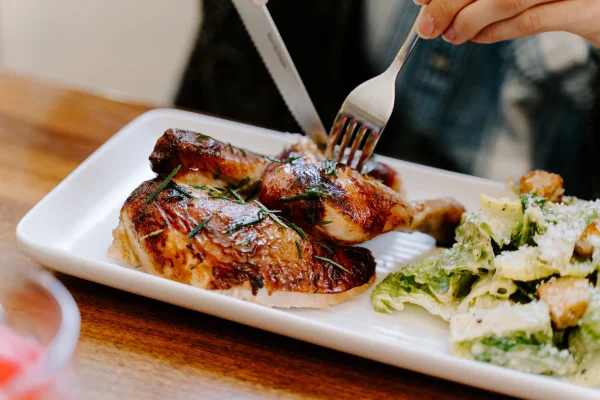 Fotografia colorida mostrando pessoa cortando pedaços de frango assado em um prato com salada-Metrópoles