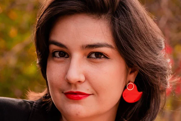 Mulher branca de óculos mostrando brinco da marca Manualmente Joias
