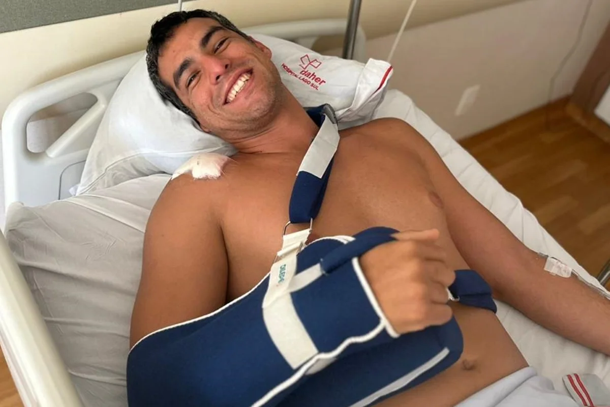 Foto colorida de homem deitado em cama hospitalar com tipóia no braço e curativo após lesão grave no ombro - Metrópoles.