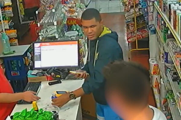 Imagem colorida de homem parto com moletom azul escuro com iogurte em caixa de supermercado - Metrópoles