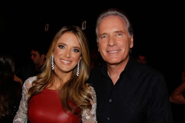 Foto colorida de Ticiane Pinheiro usando vestido vermelho e Roberto Justus usando camisa preta - Metróples