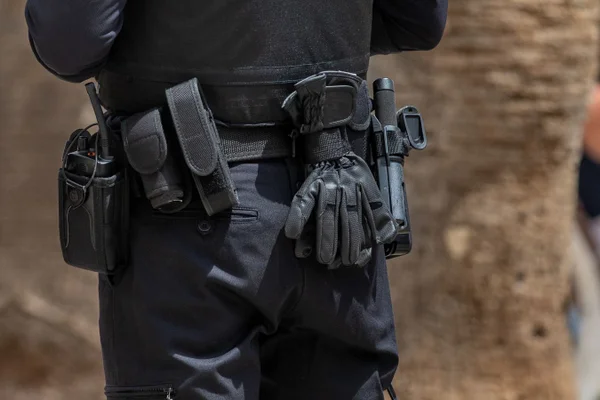 Fotografia colorida mostra cinturão de policial armado com luvas, spray, arma e cassetete