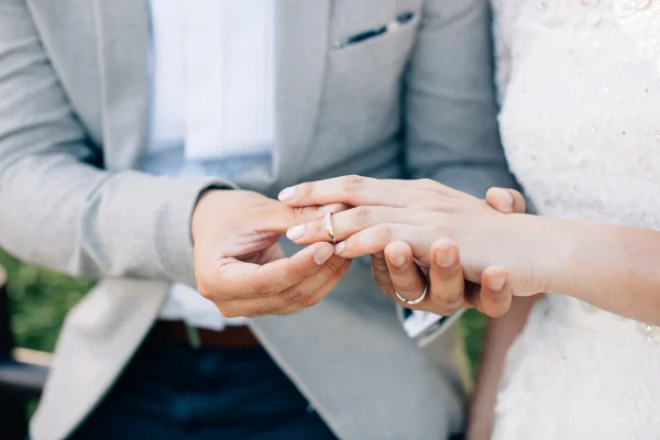 Noivo colocando aliança no dedo da noiva. Troca de alianças. Casal feliz celebrando casamento ao ar livre. Metrópoles