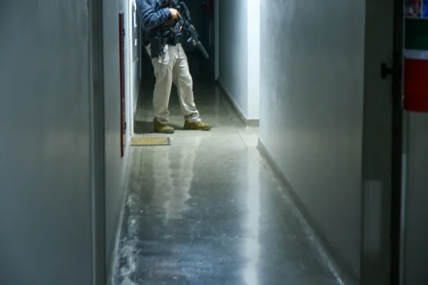 Imagem colorida de policial segurando arma. Metrópoles