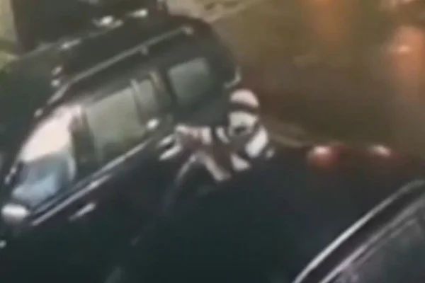 Imagem colorida de homem encapuzado com arma apontada para carro preto. Metrópoles