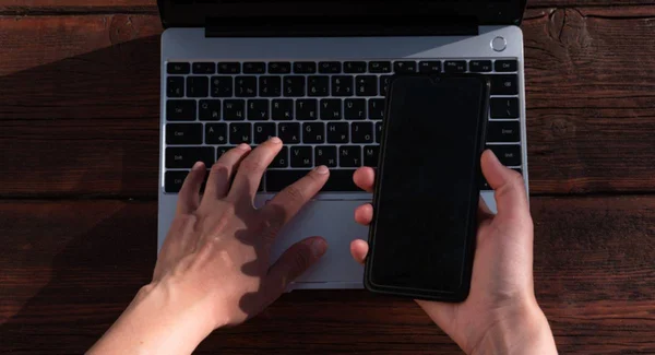 Fotografia colorida mostrando uma mão mexendo em teclado de computador e outra segurando celular-Metrópoles