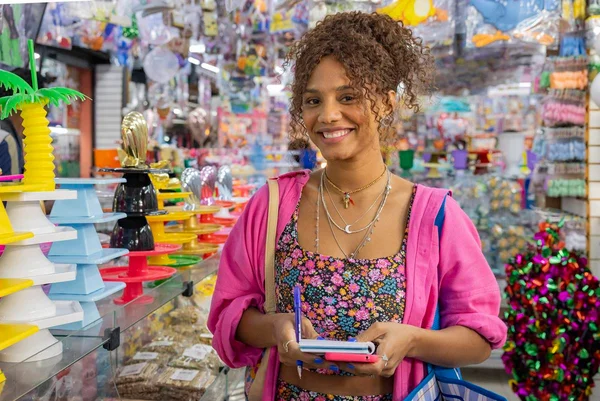 foto colorida da atriz jessica ellen, mulher negra vestida com blusa estampada e camisa rosa aberta segurando caderno - metrópoles