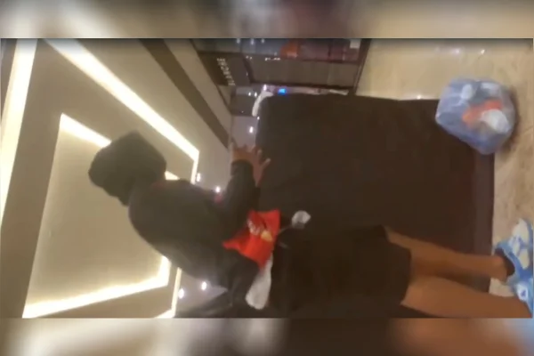 Imagem colorida de um jovem de camisa e bermuda pretas em um shopping cujas lojas ao redor estão fechadas