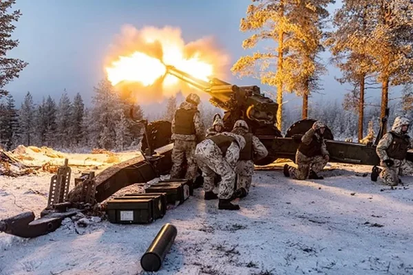 Soldados finlandeses em exercício militar se reúnem atrás de canhão em fogo. Ele estão numa floresta de pinheiros, coberta de neve - Metrópoles