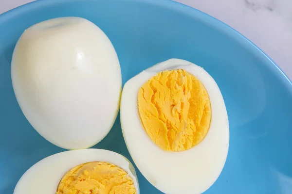 Foto colorida de ovos, sendo um inteiro e outro cortado ao meio. O alimento está em um prato azul - Metrópoles