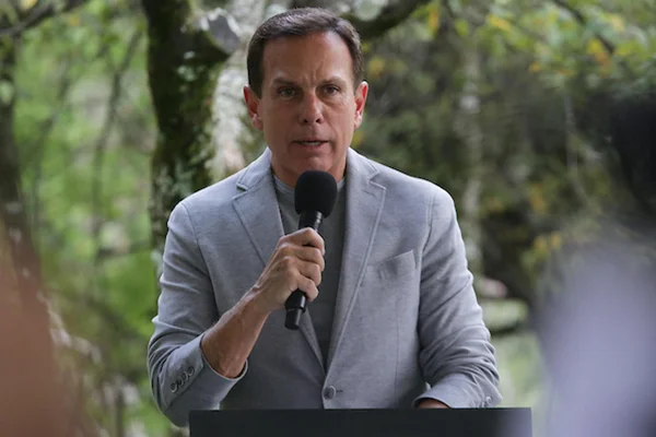 Governador de São Paulo, João Dória discursa em dia de liberação das máscaras em espaços fechados no estado. Ele usa terno cinza e fala ao microfone - Metrópoles