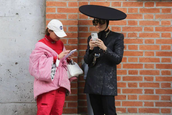 Mulher usa look vermelho com boné branco ao lado de homem com visual preto com alfaiataria e chapéu