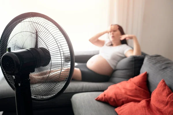 Foto colorida de mulher grávida sentada em frente a um ventilador - Metrópoles