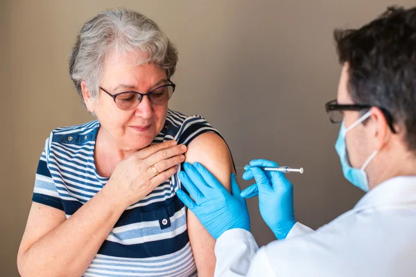 Mulher mais velha recebendo uma vacina de herpes zóster pelo médico no braço.