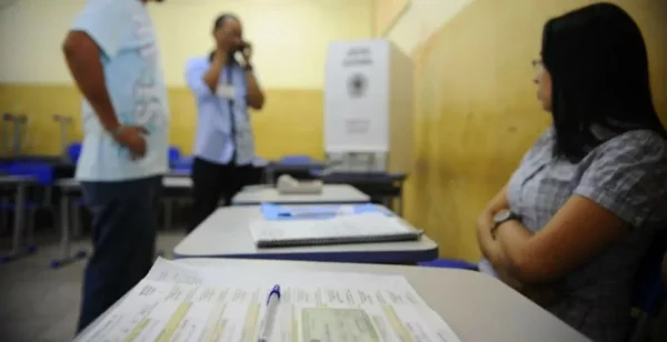 sentada à mesa, mesária auxilia eleitores
