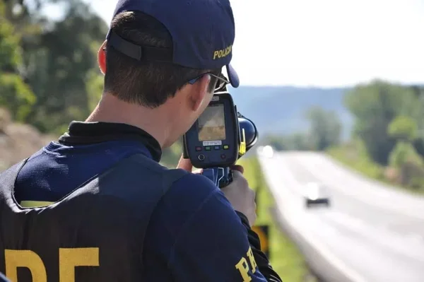 Imagem colorida de agente da PRF segurando um radar pistola - Metrópoles