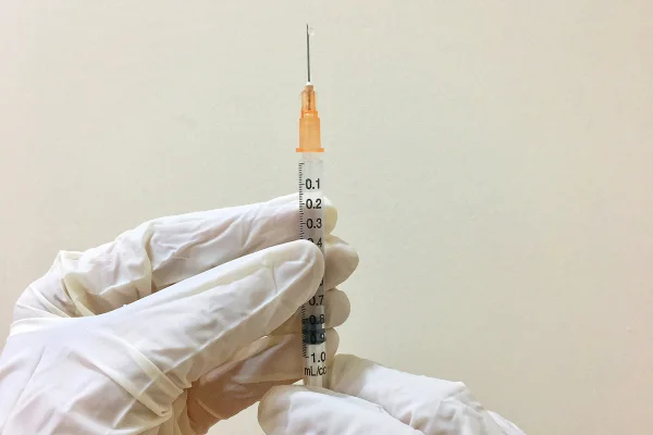 Foto colorida de pessoa com luvas de borracha segurando uma seringa de ponta laranja e agulha muito fina - Estudo: alumínio presente nas vacinas é seguro e não causa doenças - Metrópoles.