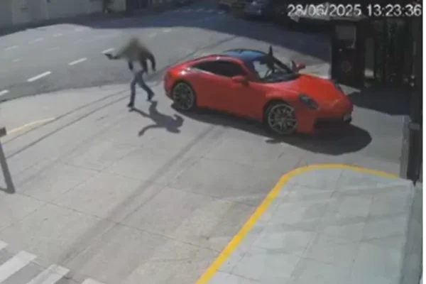Imagem colorida de um homem armado ao lado de uma Porsche vermelha no meio da rua - Metrópoles