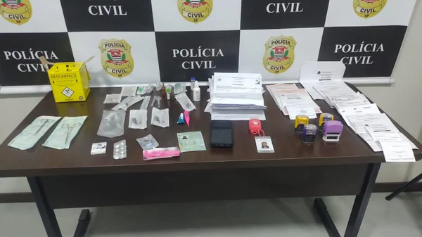 Imagem de objetos espalhados sobre mesa de delegacia (tesouras, papéis e carimbos) encontrados com mulher que vendia atestados médicos falsos - Metrópoles