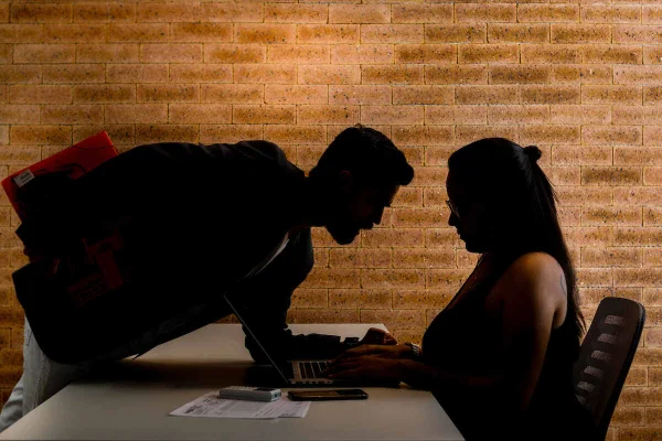 Homem se inclina sob mesa em que mulher digita em computador