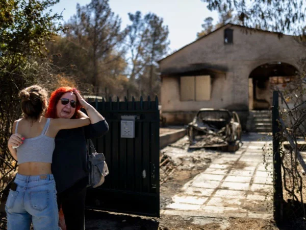 Mulher é consolada por uma menina em frente à sua casa incendiada, que foi destruída por um incêndio florestal, na Grécia - Metrópoles