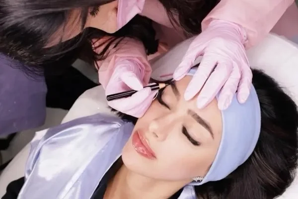 Mulher realizando procedimento de sobrancelha em outra mulher - Metrópoles