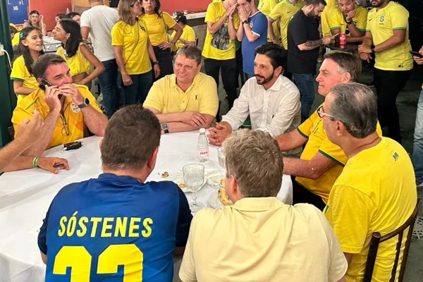 Imagem colorida mostra um bar instalado em um salão amplo, com uma mesa redonda ao centro, ocupada por ricardo nunes, jair bolsonaro, tarcísio de freitas e outros políticos, todos vestidos de amarelo - Metrópoles