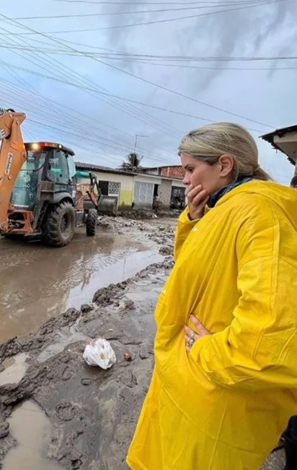 mulher de capa de chuva amarela posa chocada em rua cheia de lama - metrópoles