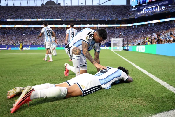 Foto colorida de jogador da Argentina deitado em gramado e outro atleta fala com ele - Metrópoles