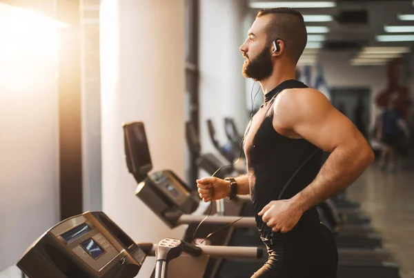 Foto mostra homem musculoso e de barba correndo em esteira cardio