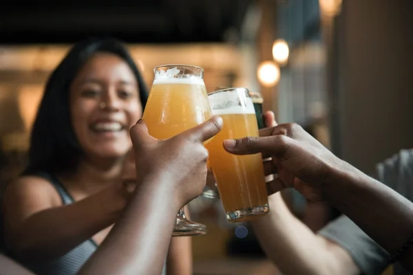 Foto com várias pessoas segurando copos com cerveja e brindando, Metrópoles.