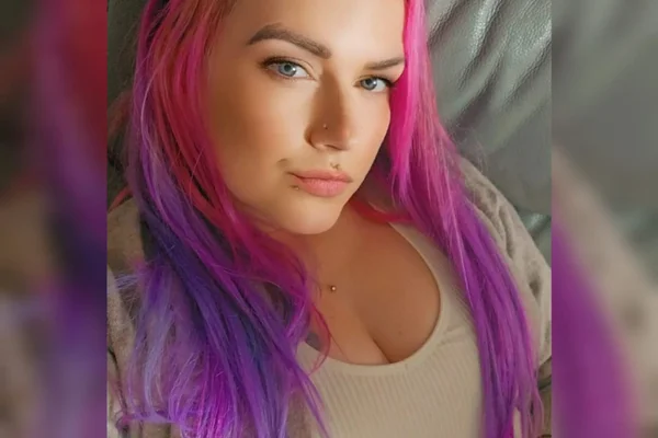 Foto mostra uma mulher branca de olhos azuis e com o cabelo colorido em um degradê de rosa ao roxo. É Jade Williams, mulher que descobriu que sua menstruação intensa era fruto do fato de ter útero duplo - Metrópoles
