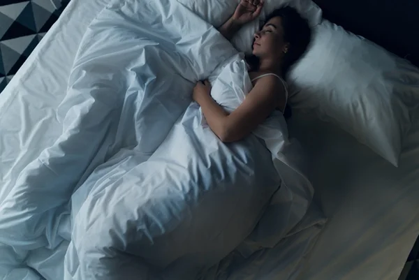 Foto colorida de mulher dormindo em cama com cobertor - Metrópoles