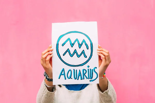 foto de uma pessoa segurando papel escrito aquarius com fundo rosa