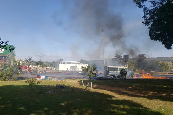 Fumaça e fogo saindo de van em pista ao lado de gramado