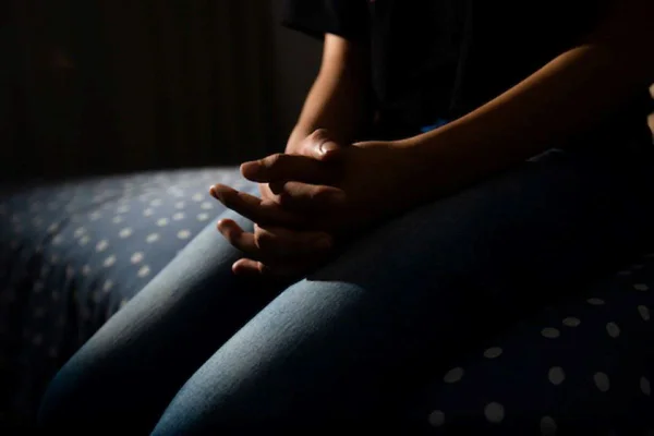 Imagem mostra corpo de menina jovem no escuro com as mãos entrelaçadas - Metrópoles