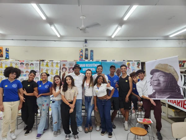 imagem colorida mostra estudantes em escola pública de são paulo. eles estão em uma biblioteca e seguram uma imagem do cantor milton nascimento - metrópoles