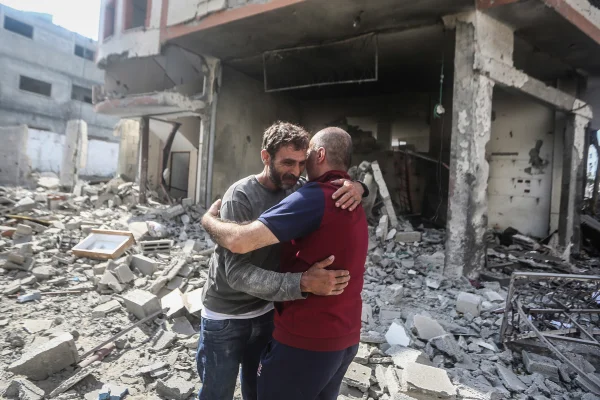 Homens palestinos confortam uns aos outros enquanto inspecionam o bairro devastado de Karama após o bombardeio israelense na Cidade de Gaza