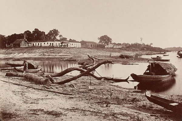 Paisagem em preto e branco, com um casarão ao fundo e um lago parcialmente seco com um barco em primeiro plano - Metrópoles