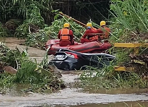Imagem de três bombeiros em cima de um bote próximo a um carro preto submerso - Metrópoles