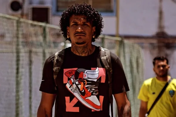 foto colorida de homem negro de cabelos cacheados vestido em camiseta preta - metrópoles